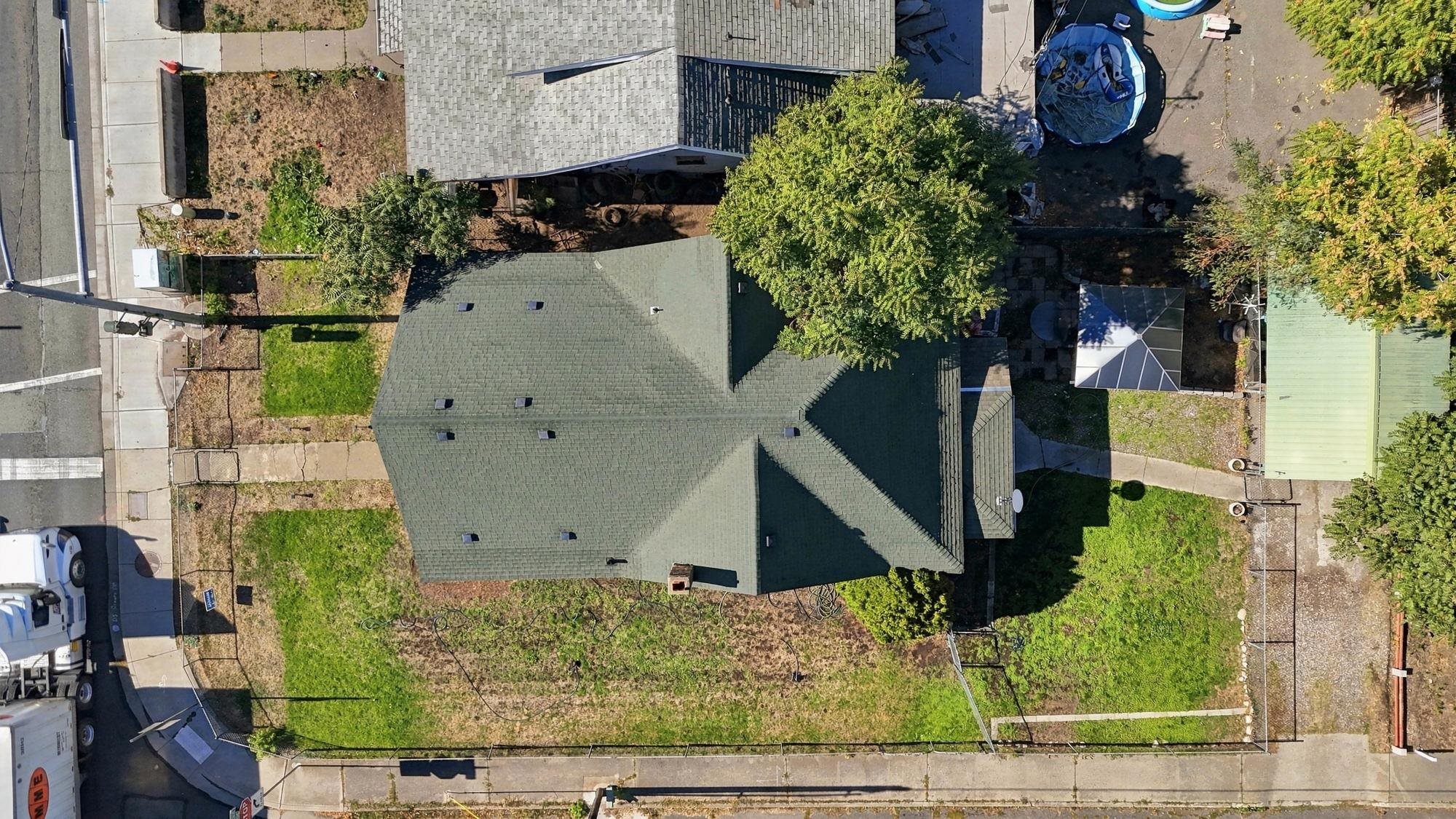 Aerial view of a house and fenced yard with mature trees and neighboring homes.
