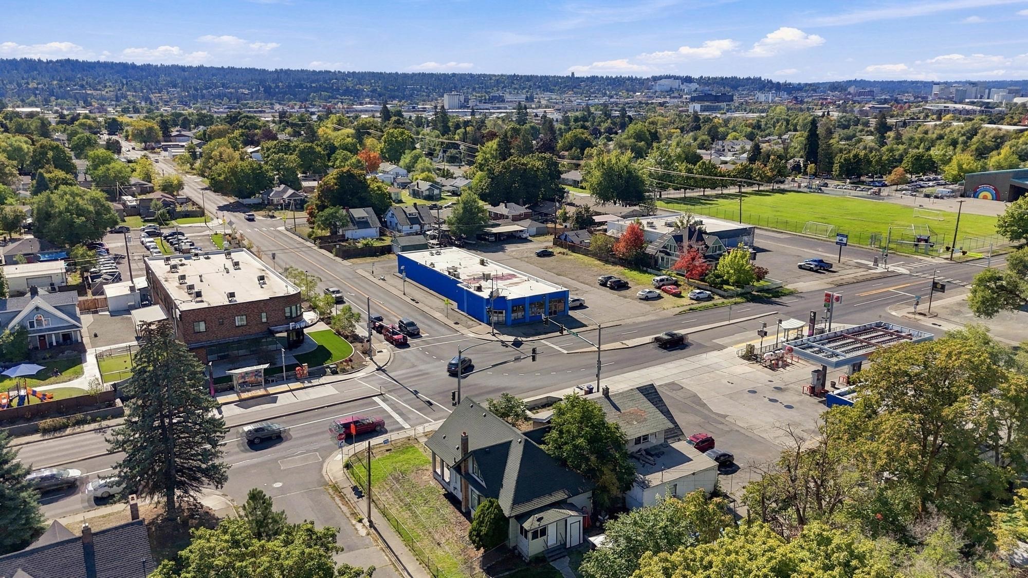 Aerial view of a Spokane neighborhood with tree-lined streets, a sports field, and distant city buildings.