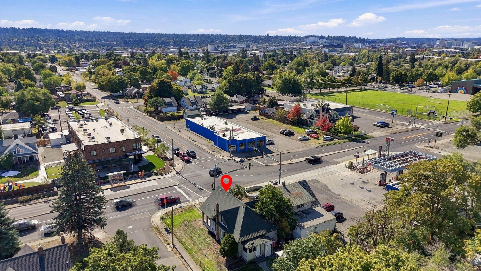 Aerial neighborhood view with a red pin marking a house near a busy intersection and green sports field.