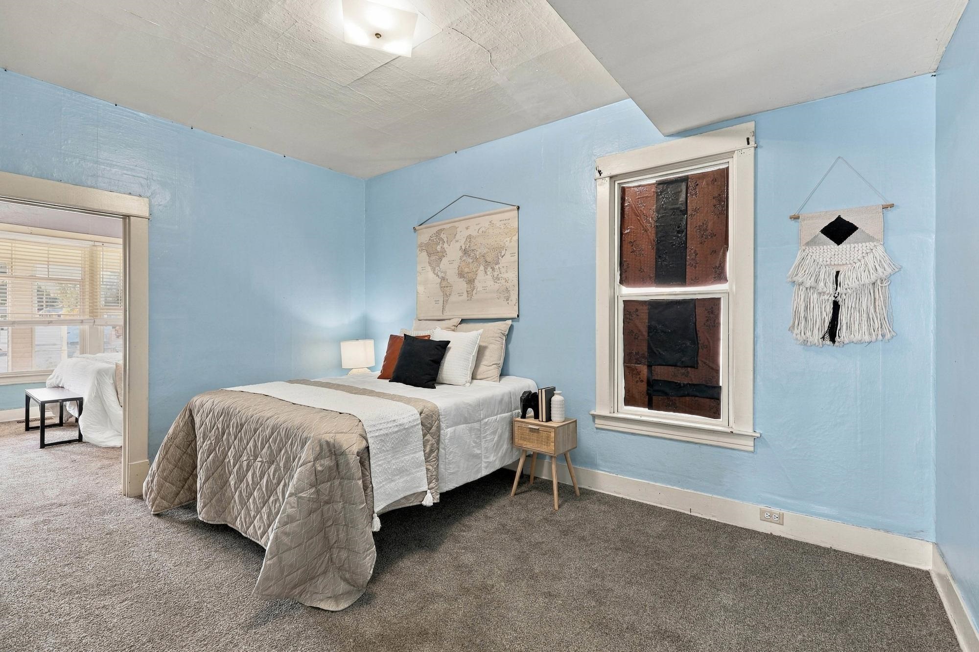 Furnished bedroom with blue walls, a white-and-taupe bed, and a world map above the headboard.