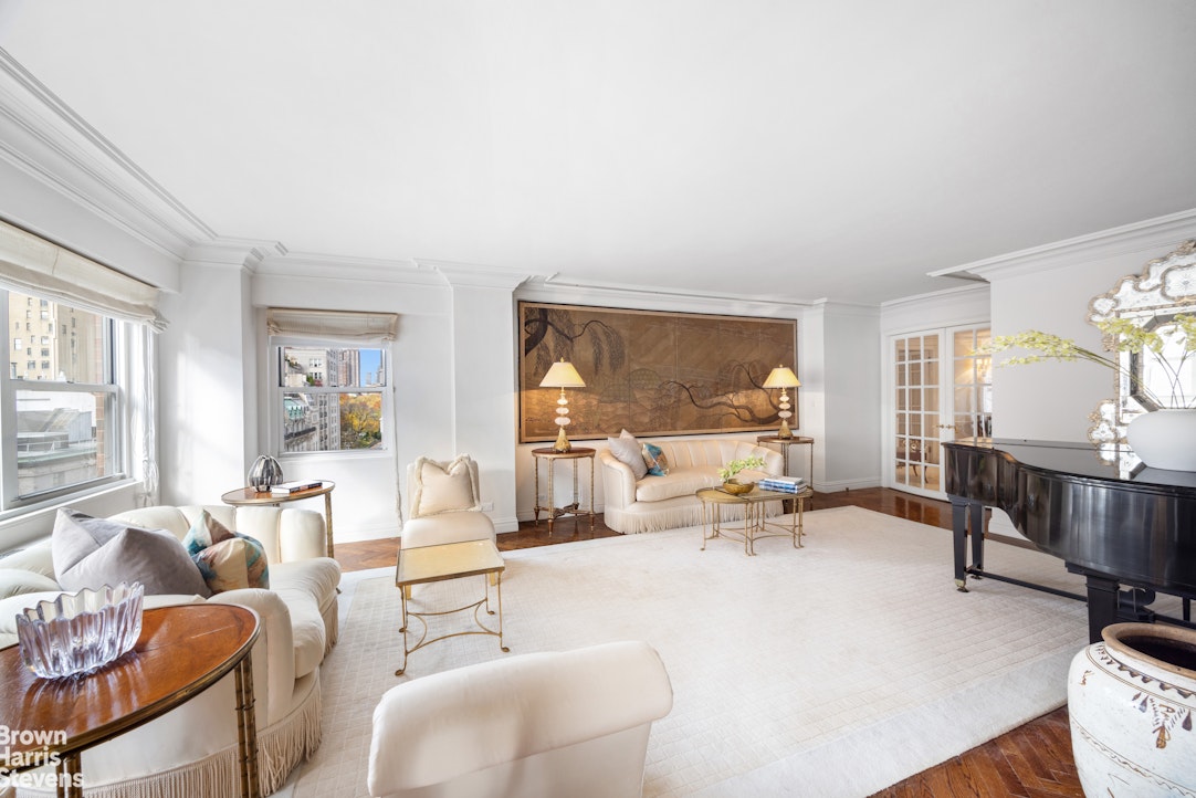 Living room with white seating, a grand piano, and large windows overlooking city buildings.