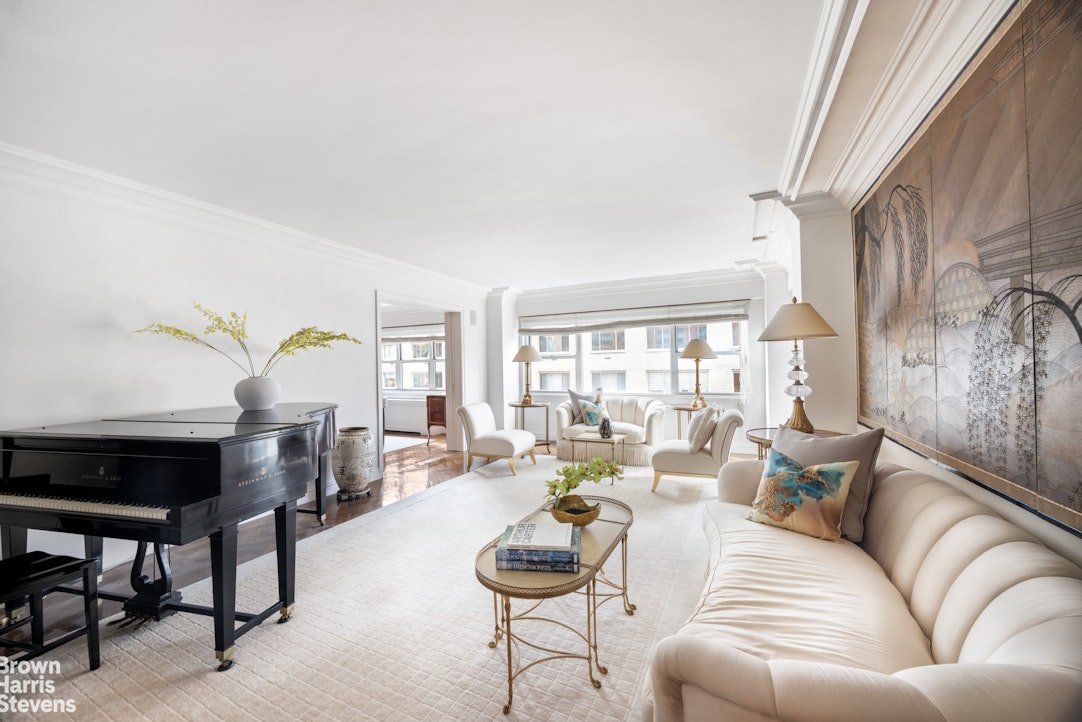Living room with a black grand piano, ivory seating, and large windows overlooking neighboring buildings.