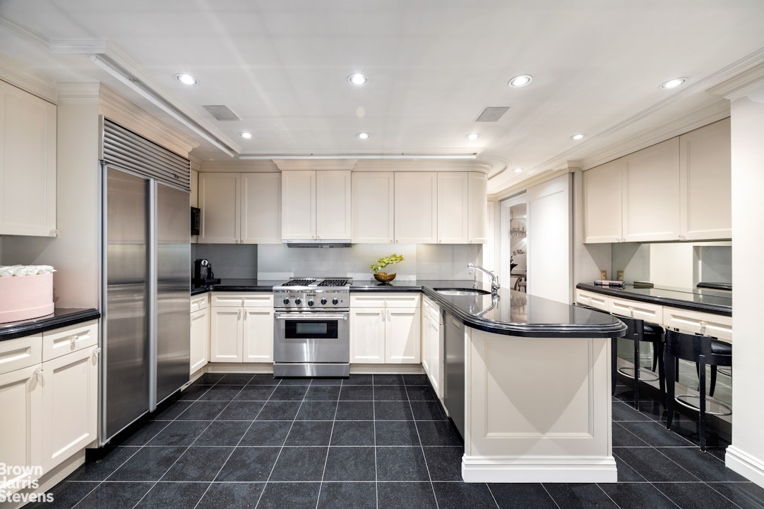 Kitchen with white cabinetry, stainless steel appliances, and a curved black island.