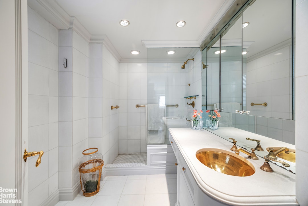 Bathroom with a glass-enclosed shower and white vanity topped by a brass vessel sink.