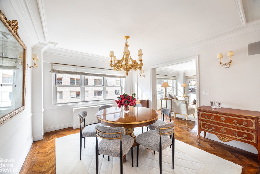 Dining room with a round wood table, gray chairs, gold chandelier, and parquet floors.
