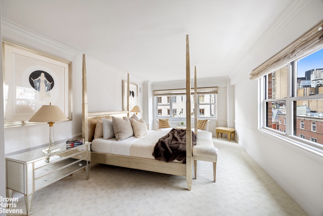 Bright bedroom with a four-poster bed and large windows overlooking city buildings.