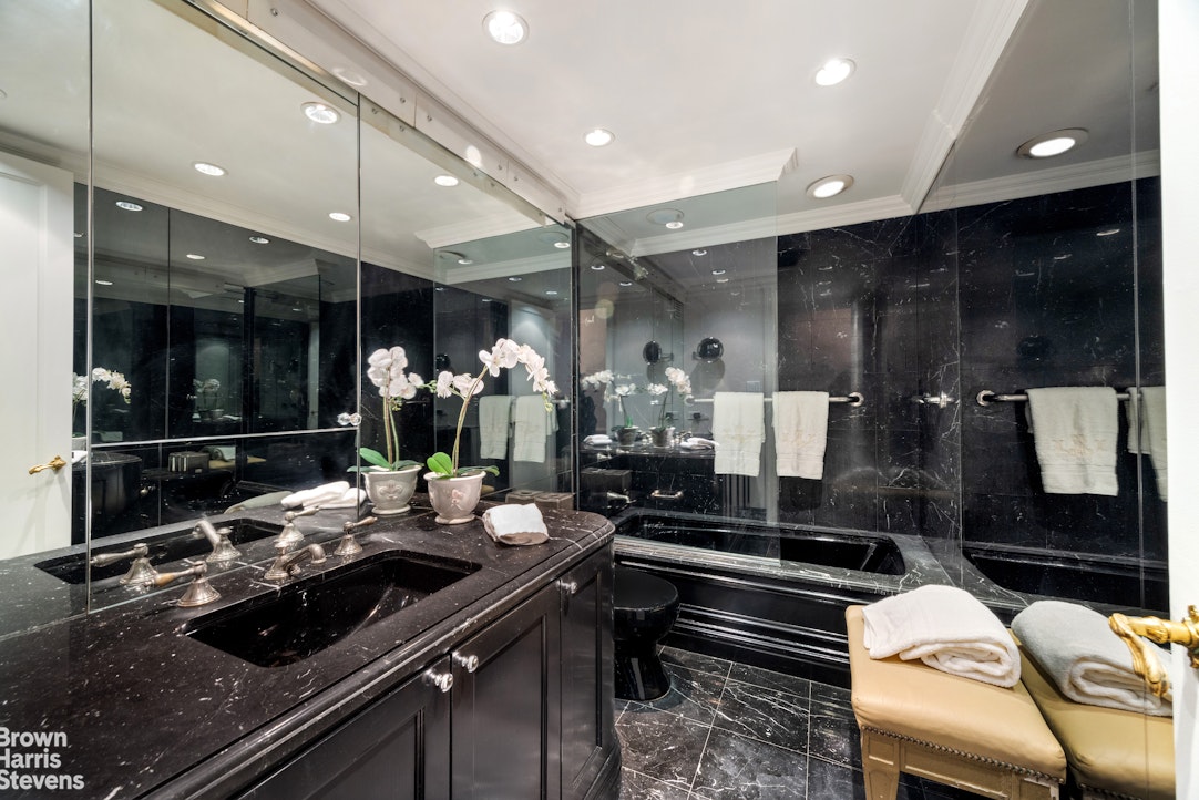 Bathroom with black marble surfaces, a mirrored wall, bathtub, and orchid-topped vanity.