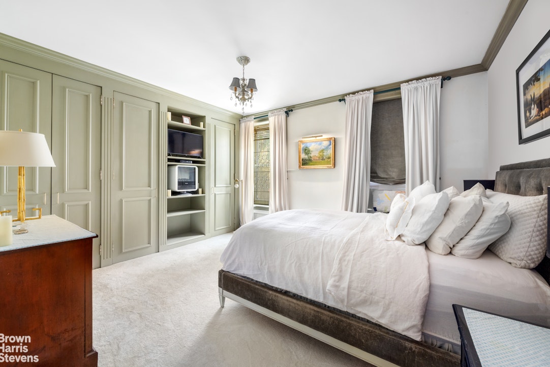 Bedroom with a white bed, pale green paneled cabinets, and curtained windows.