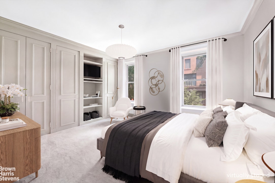 Staged bedroom with a white bed, paneled cabinetry, and tall curtained windows.