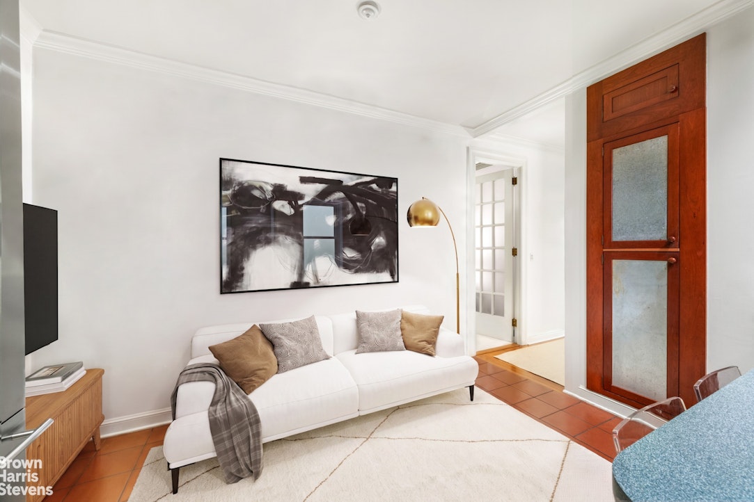 Living room with a white sofa, abstract artwork, terracotta tile floor, and brass floor lamp.