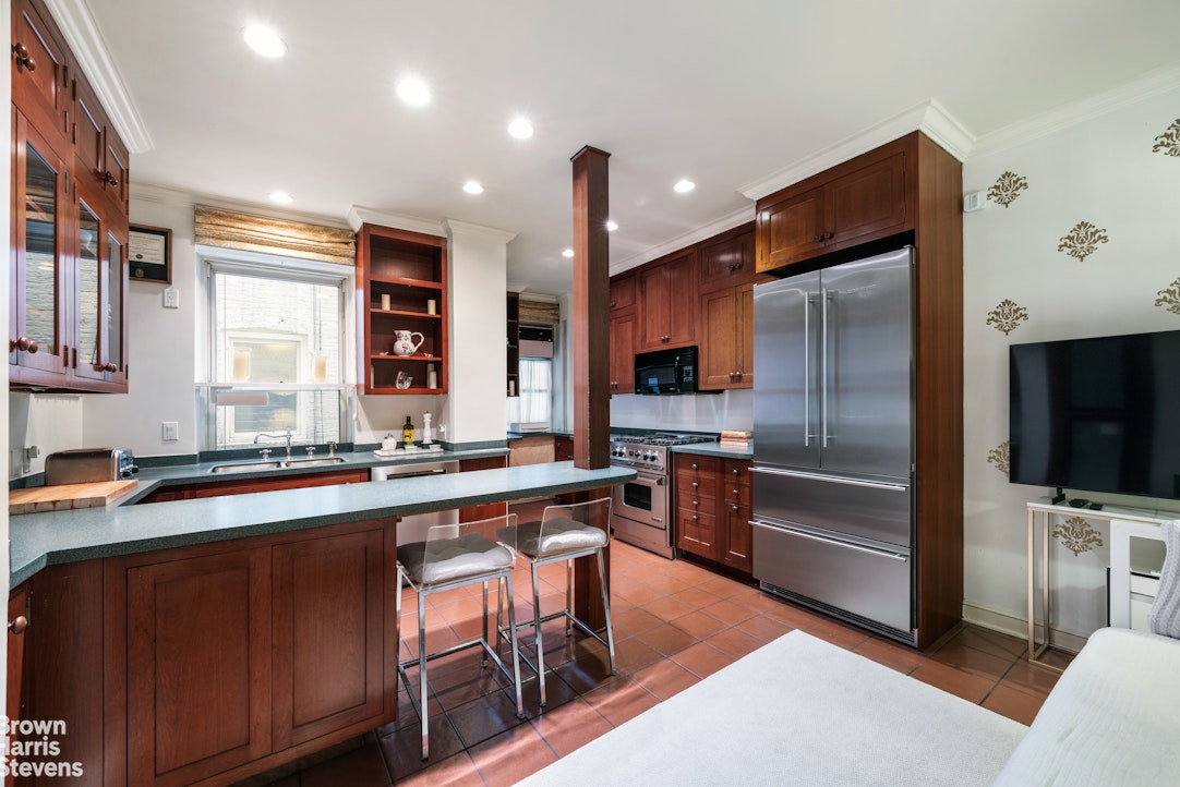 Kitchen with dark wood cabinets, a green stone island, stainless steel refrigerator, and terracotta tile floor.