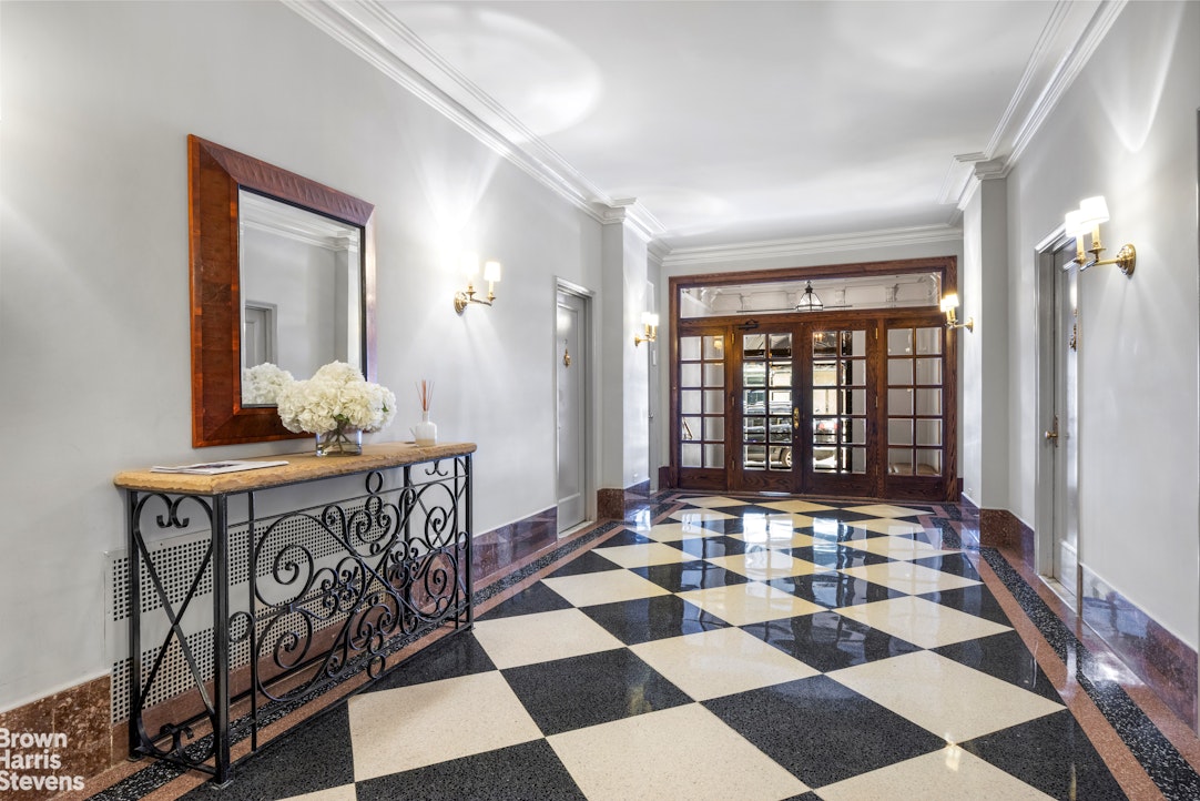 Residential lobby with a checkerboard marble floor, dark wood entry doors, and a console table.