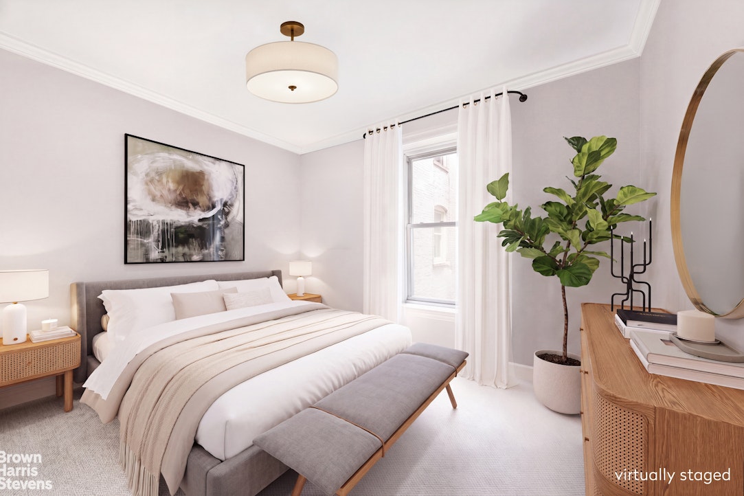 Staged bedroom with a gray upholstered bed, white bedding, and a tall window framed by white curtains.