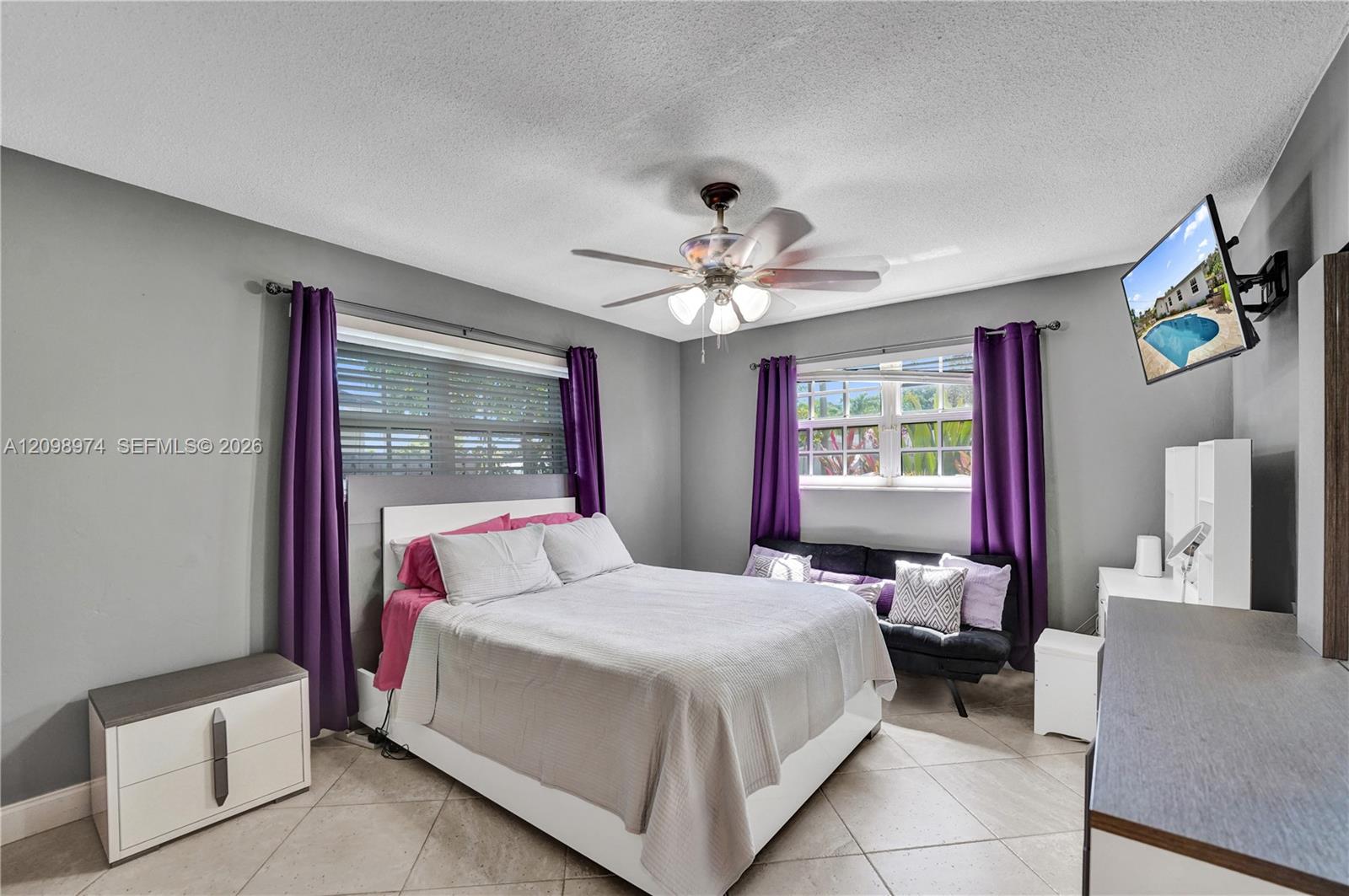 Furnished bedroom with a large white bed, purple curtains, and a sofa beneath the window.
