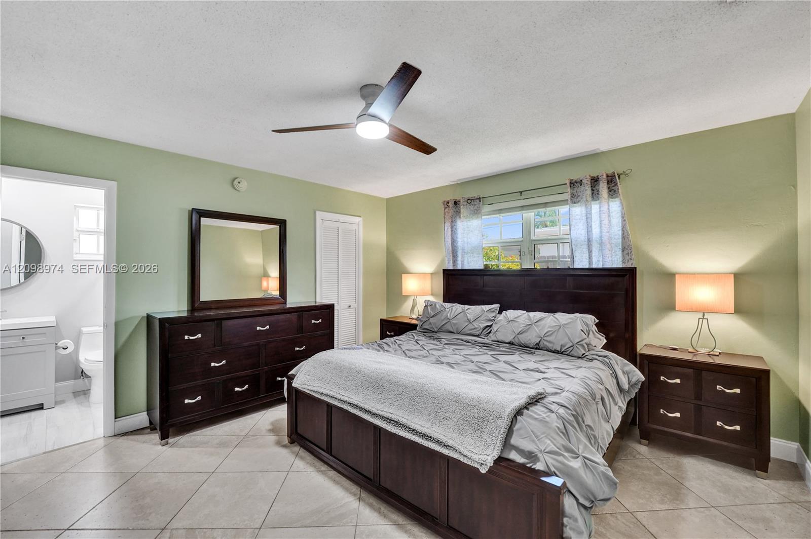 Furnished bedroom with dark wood furniture, gray bedding, pale green walls, and an adjoining bathroom.
