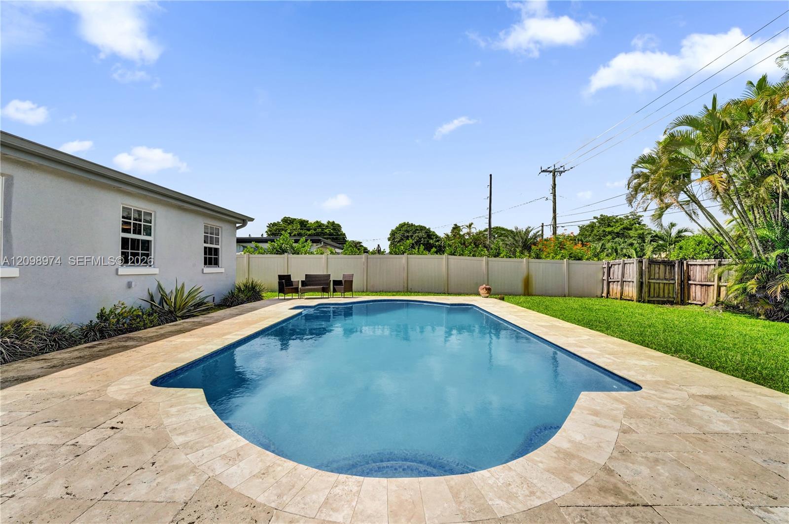 Backyard swimming pool with stone patio, lawn, privacy fence, and tropical landscaping.