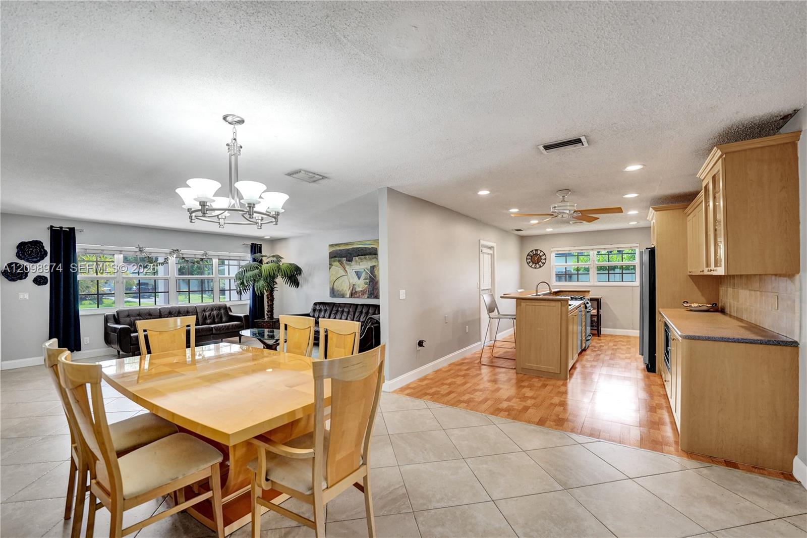 Open-plan dining area with a light wood table, black leather sofas, and an adjoining kitchen.