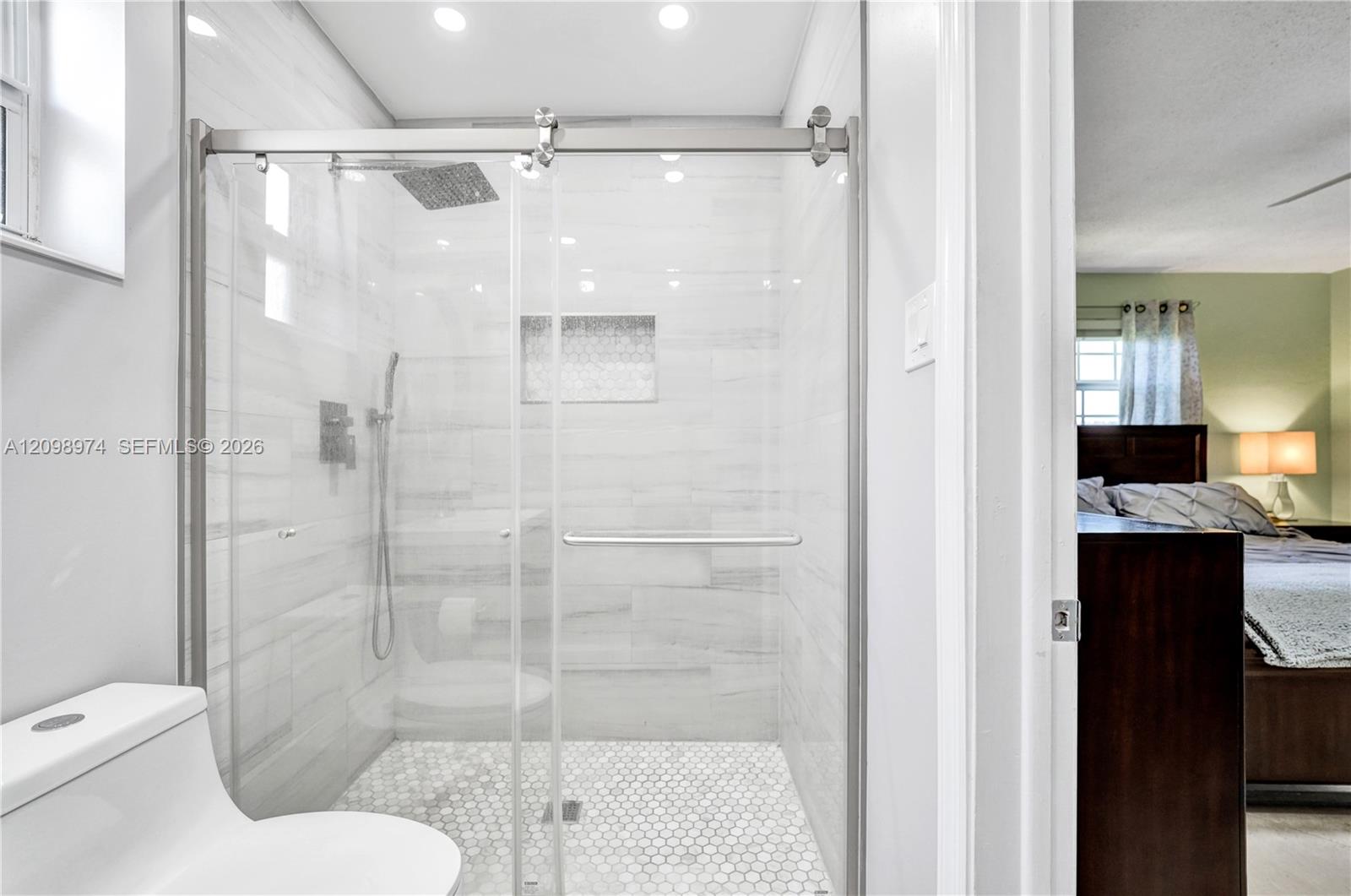 Bathroom with a spacious glass walk-in shower, marble-look tile, and hexagonal mosaic floor.