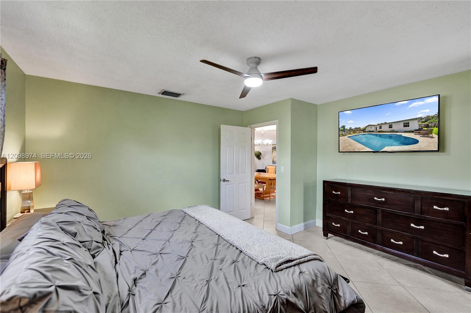 Bedroom with pale green walls, a gray bed, dark wood dresser, and ceiling fan.