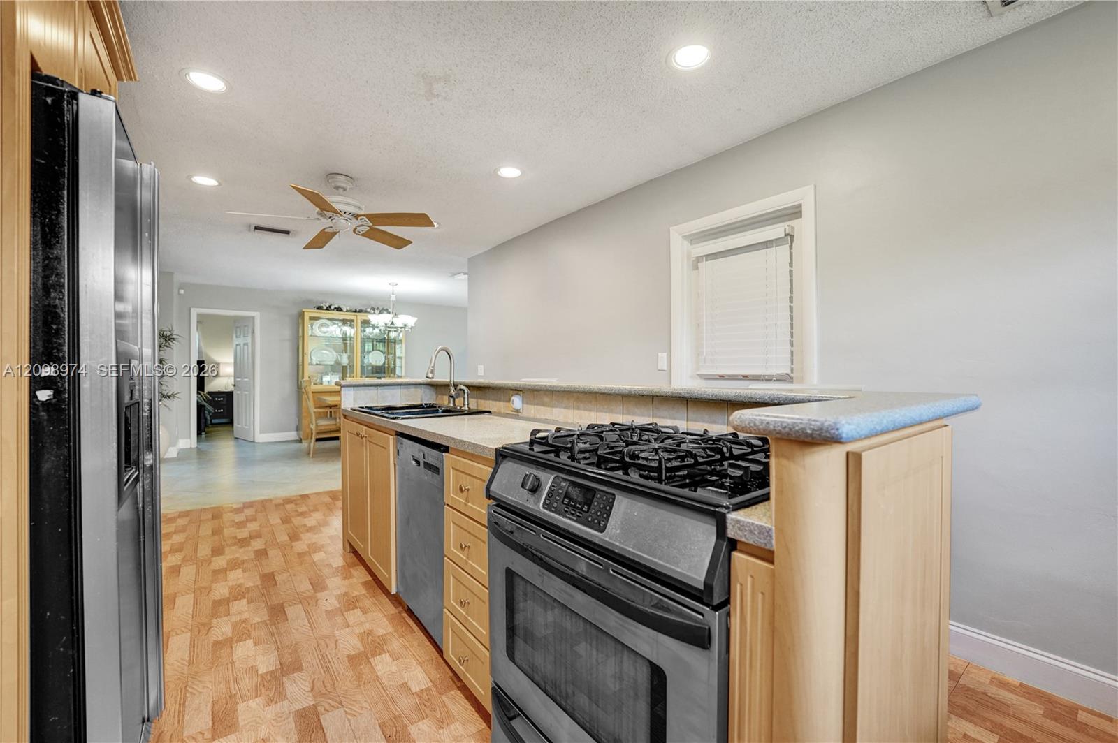 Kitchen with light wood cabinets, stainless steel appliances, and a gas range beside a breakfast bar.