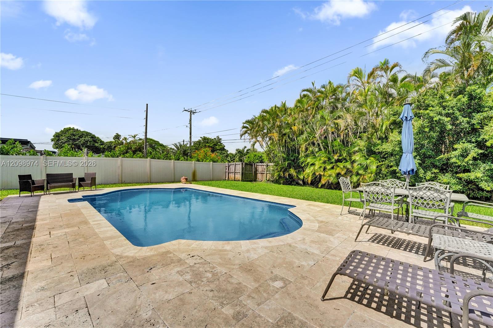 Backyard pool with a stone patio, lounge chairs, and tropical landscaping.