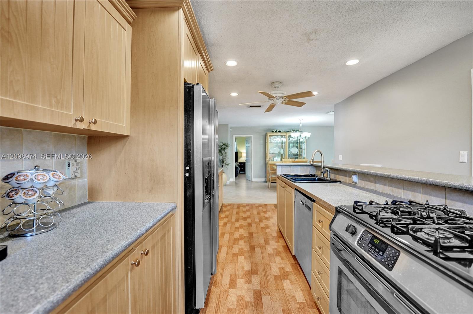 Kitchen with light wood cabinets, gray counters, stainless steel appliances, and wood flooring.
