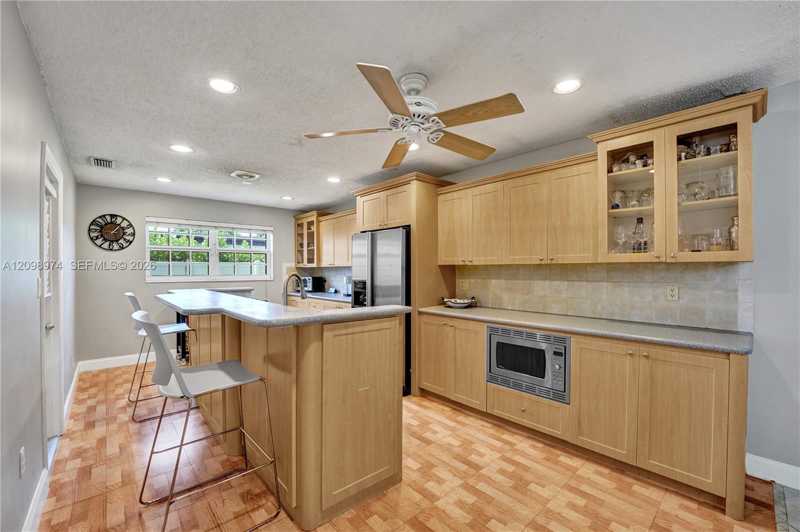 Kitchen with light wood cabinetry, glass-front cabinets, and a long peninsula with bar stools.