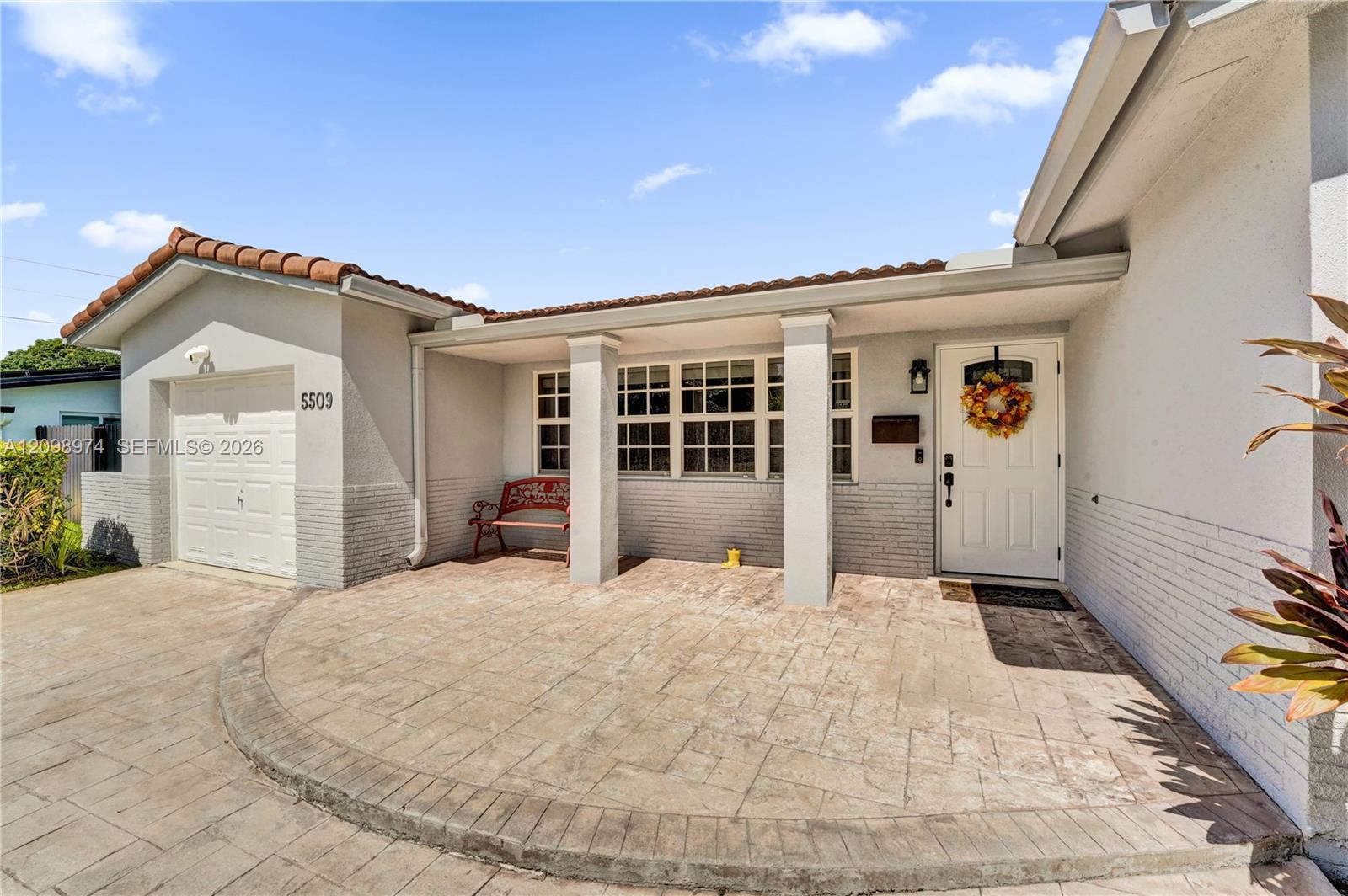 Single-story house with a covered entry, red bench, attached garage, and broad stamped-concrete driveway.