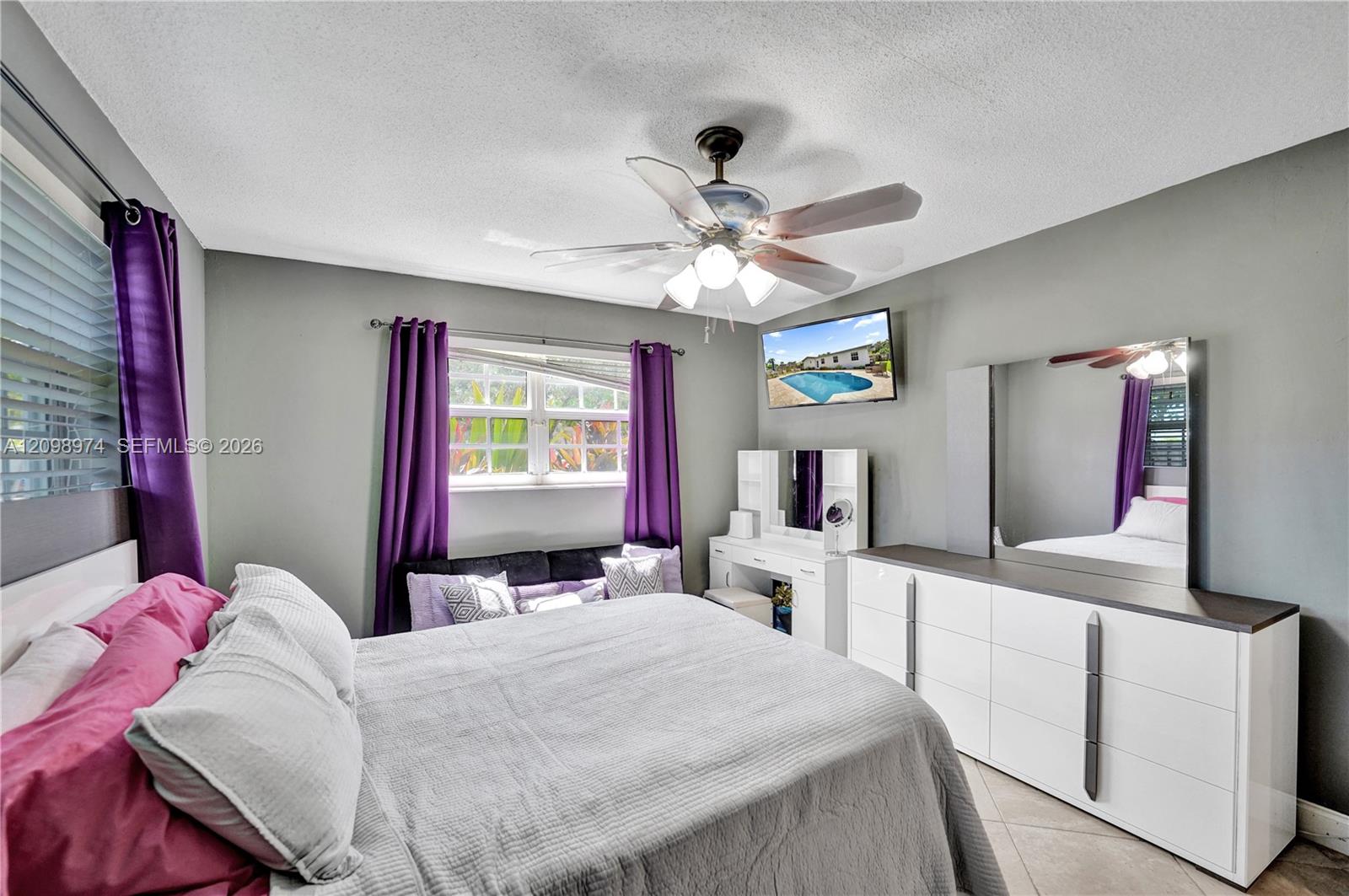 Furnished bedroom with purple curtains, a large bed, and white dressers.