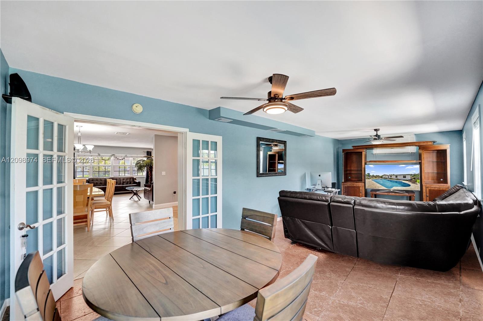 Dining and living area with an oval wood table, blue walls, French doors, and a dark leather sectional.