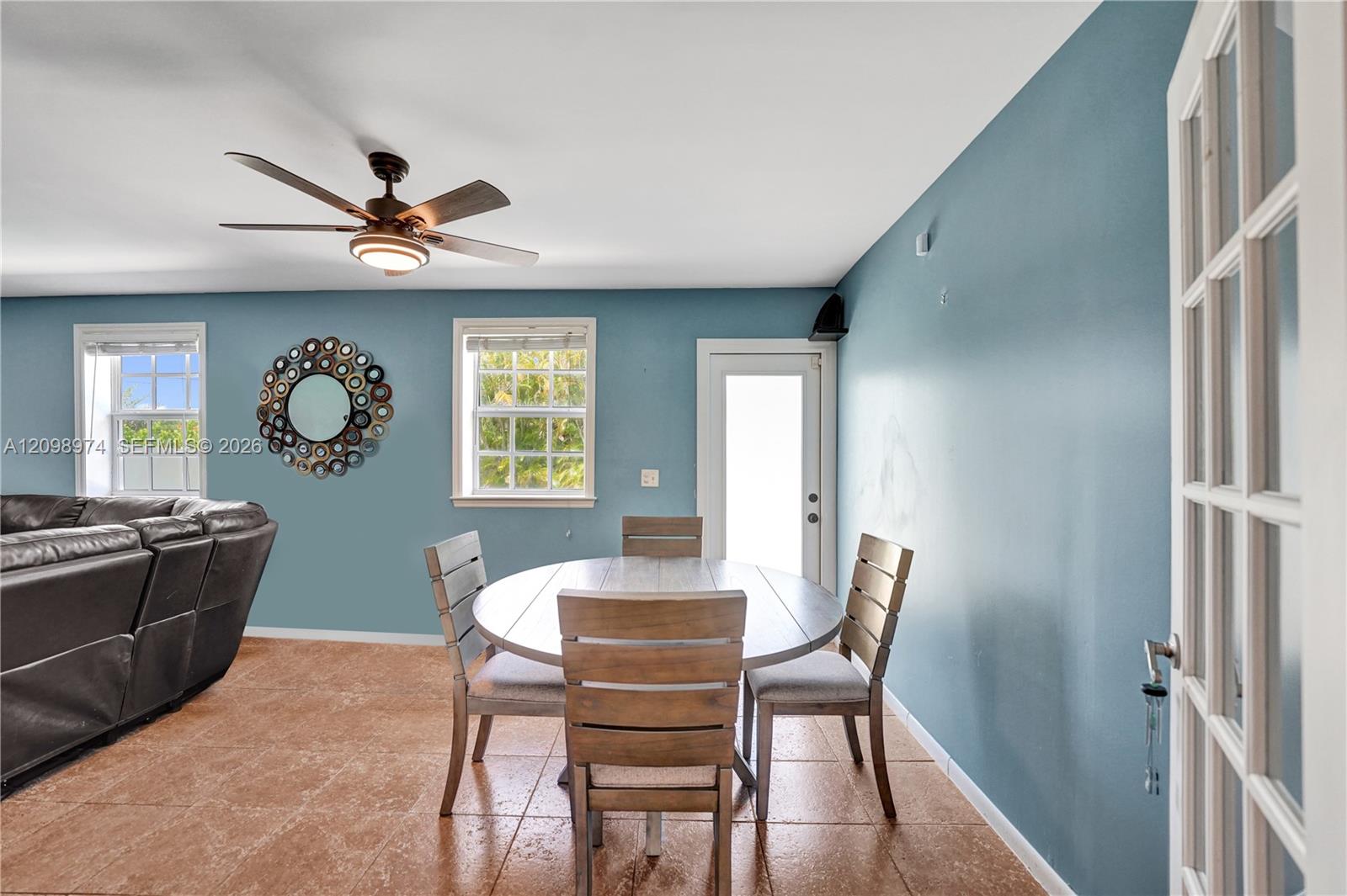 Dining area with an oval wooden table, blue walls, tile floors, and a ceiling fan.