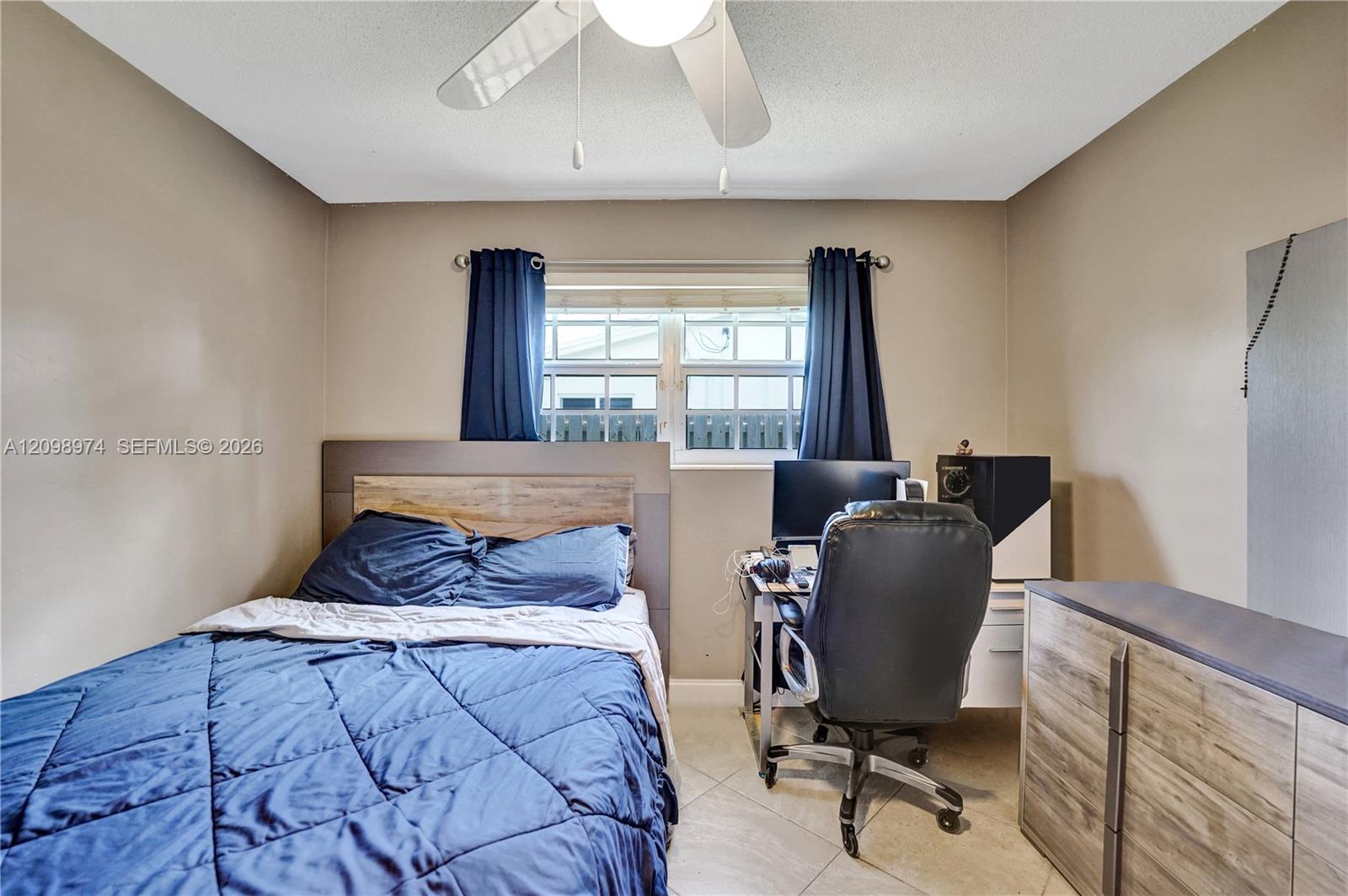 Bedroom with a blue quilted bed, desk and office chair, and navy curtains.