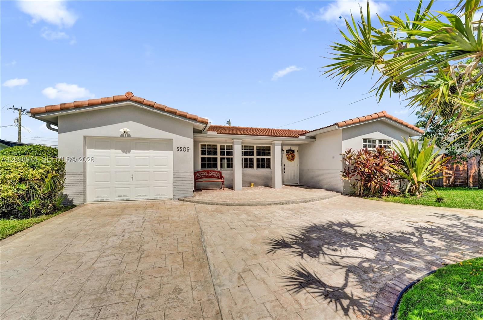 Single-story stucco house with a terracotta tile roof, attached garage, and broad driveway.
