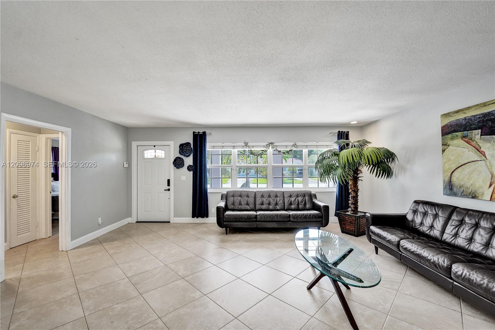 Living room with black leather sofas, a glass coffee table, and a large curtained window.