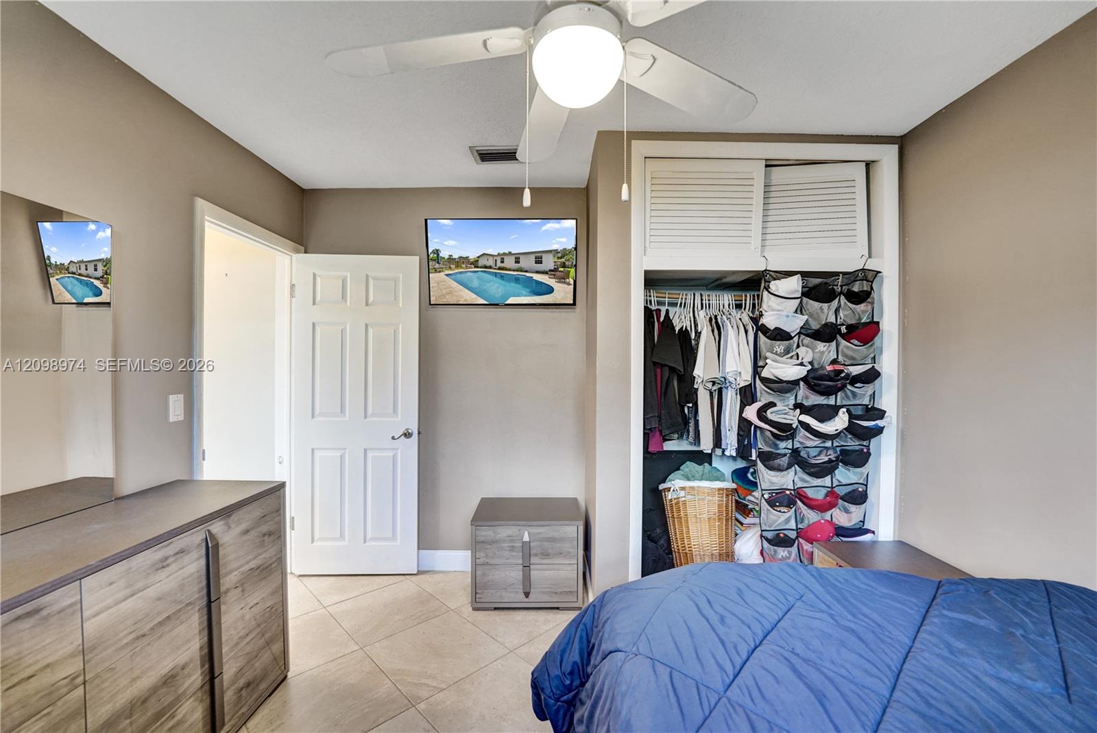 Bedroom with a blue bedspread and open closet organized with clothes and hats.