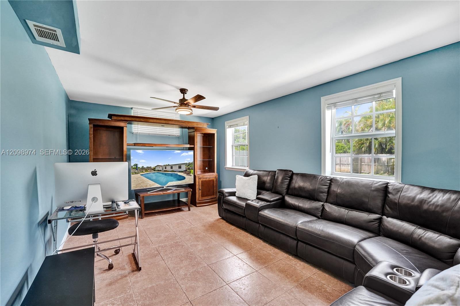 Furnished living room with blue walls, leather sectional, tiled floor, and wooden entertainment center.