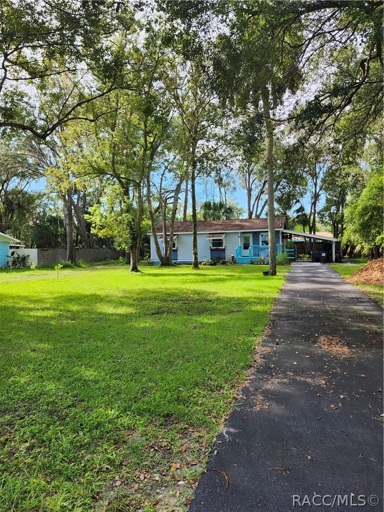 Light-blue single-story home with a turquoise porch, broad lawn, and tree-lined driveway.