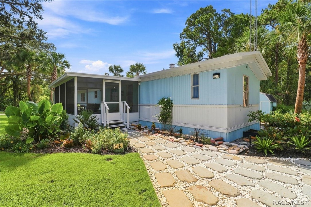 Light blue home with a screened porch, tropical landscaping, and a stone walkway.