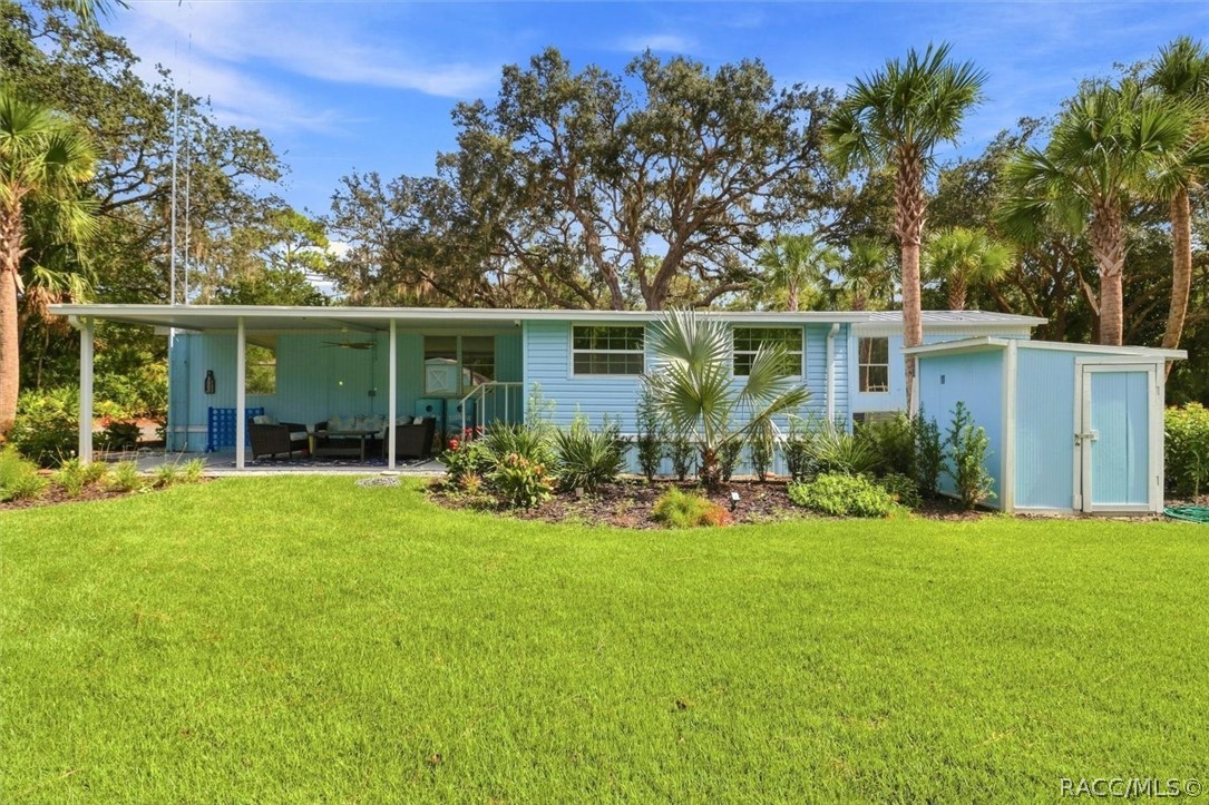Light-blue home with a covered patio, detached shed, and palm-lined lawn.