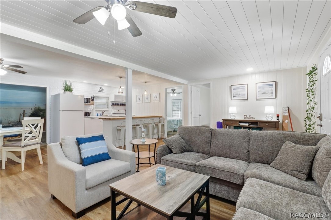Furnished living room with a gray sectional, white paneled ceiling, and open kitchen.