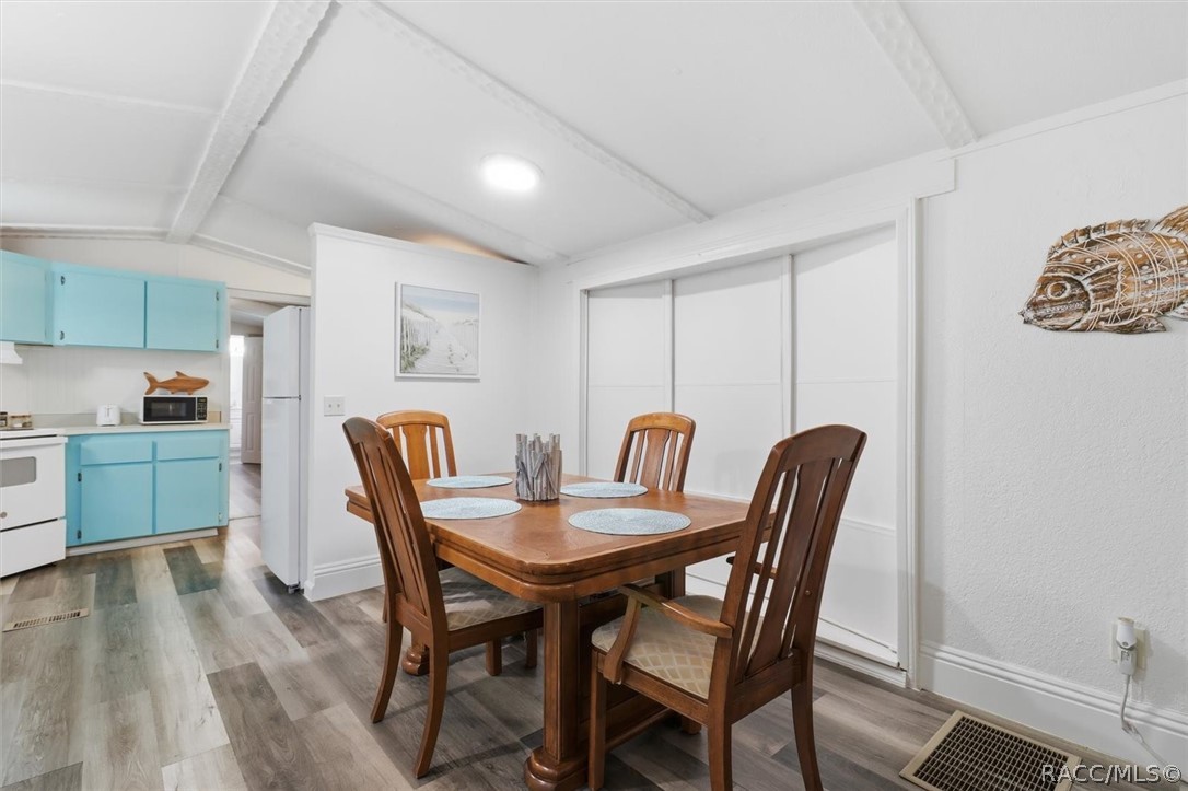 Dining area with a wooden table beside an adjoining kitchen with turquoise cabinets.