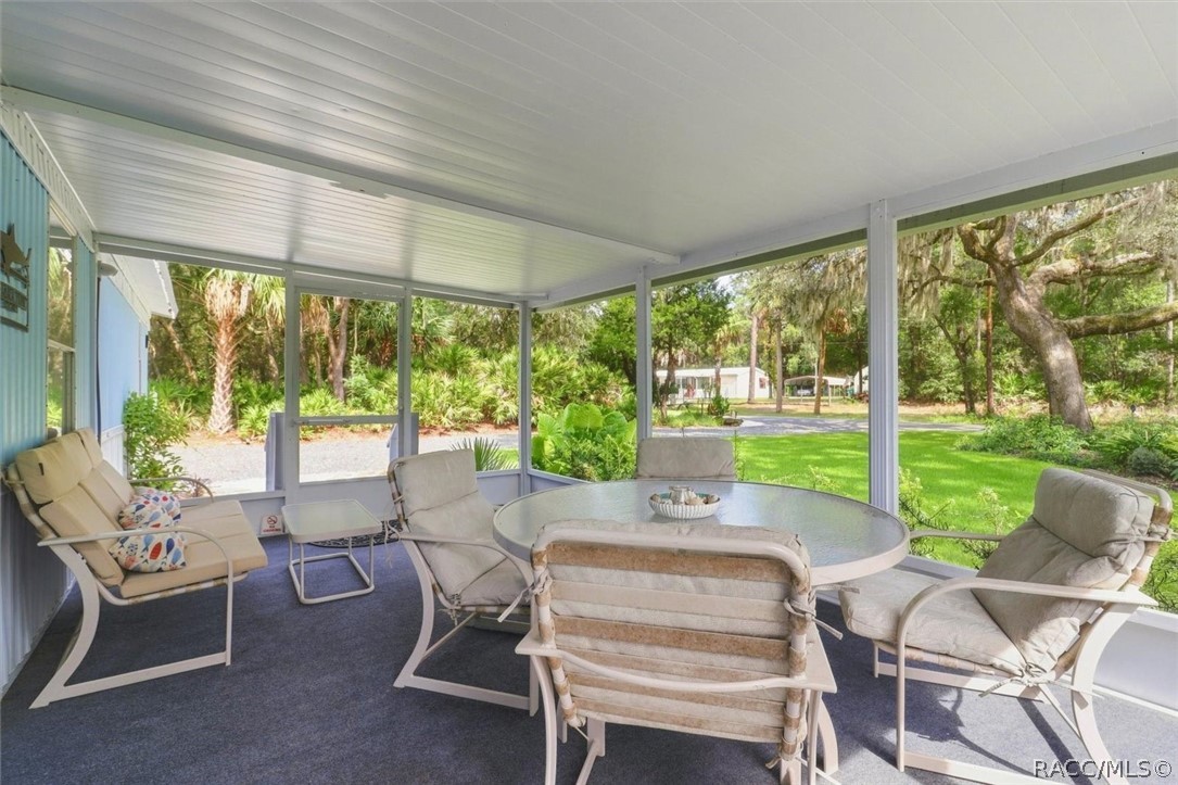 Furnished screened porch with a round glass-top table overlooking a green lawn and mature trees.