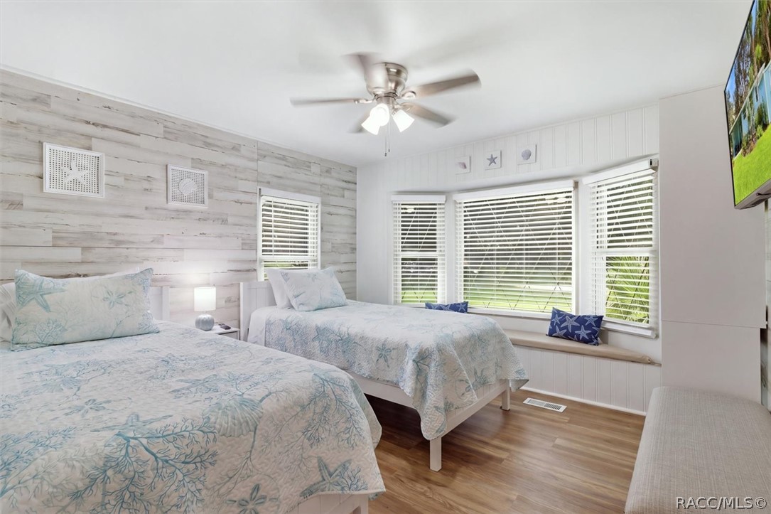 Bedroom with two pale blue floral beds, whitewashed wood accent wall, and a wide window seat.