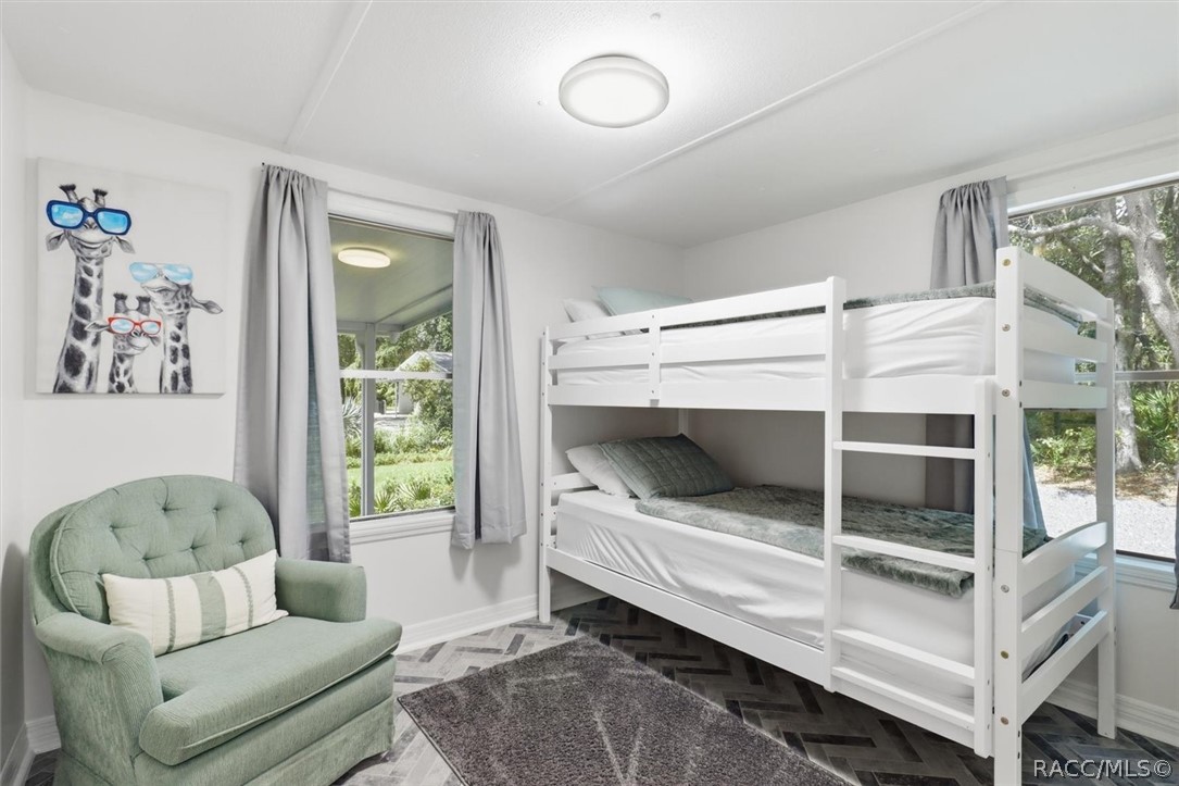 Bedroom with white bunk beds, a pale green armchair, and windows overlooking greenery.