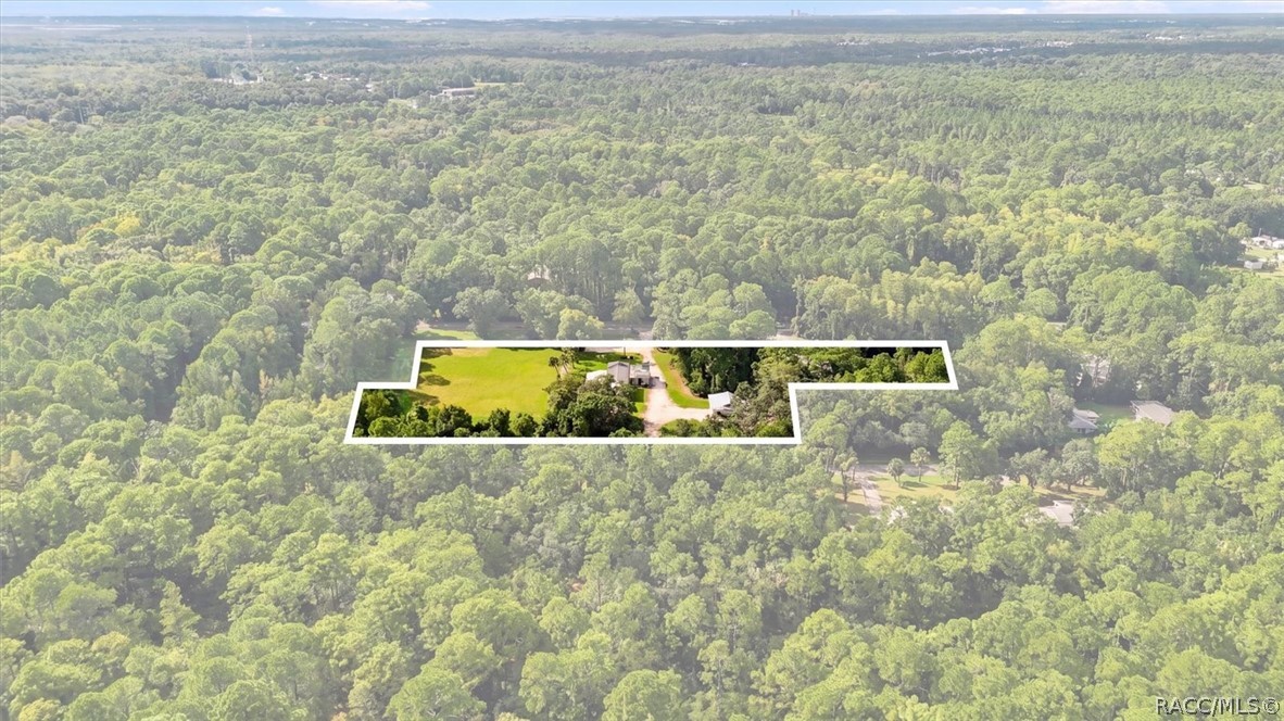 Aerial view of a wooded property with a cleared homesite, house, driveway, and outlined parcel.