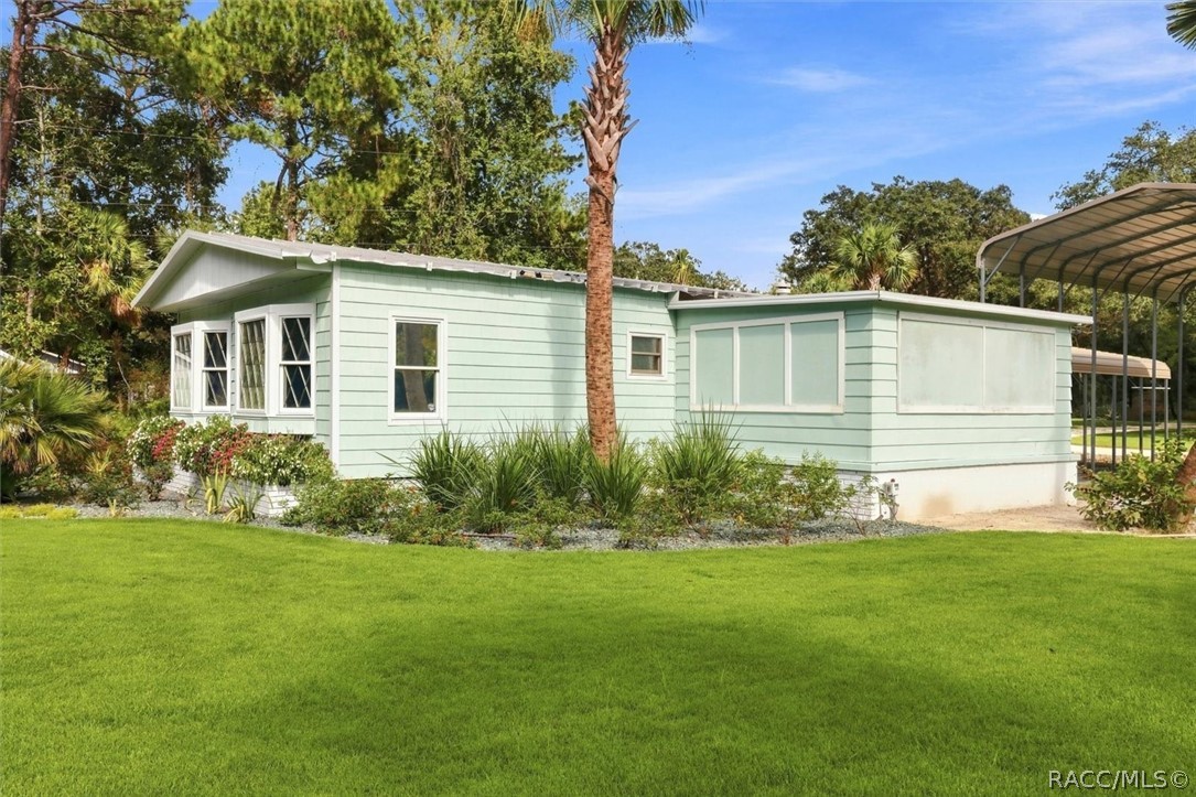 Pale mint-green home with a broad lawn, palm tree, and covered carport.