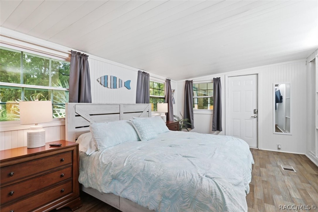 Bedroom with a large bed, white paneling, gray curtains, and windows overlooking greenery.