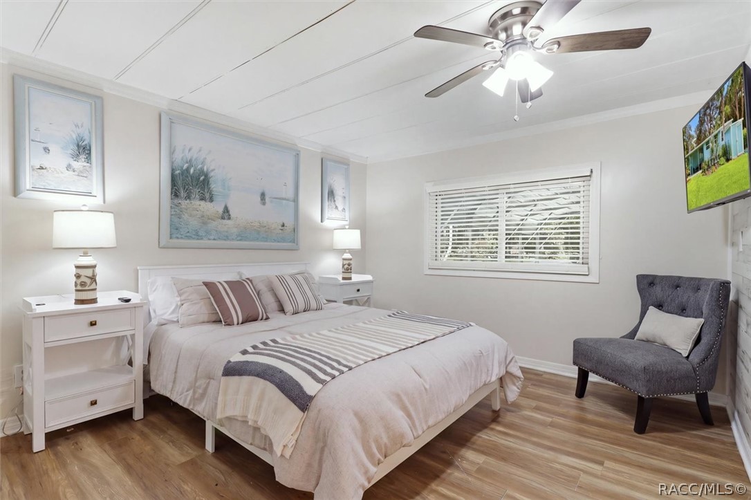 Furnished bedroom with neutral striped bedding, coastal artwork, and a gray chair.