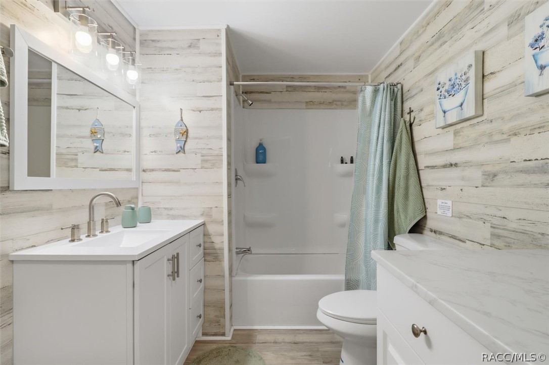 Bathroom with a white vanity, tub and shower, and pale aqua curtain against whitewashed wood-look walls.
