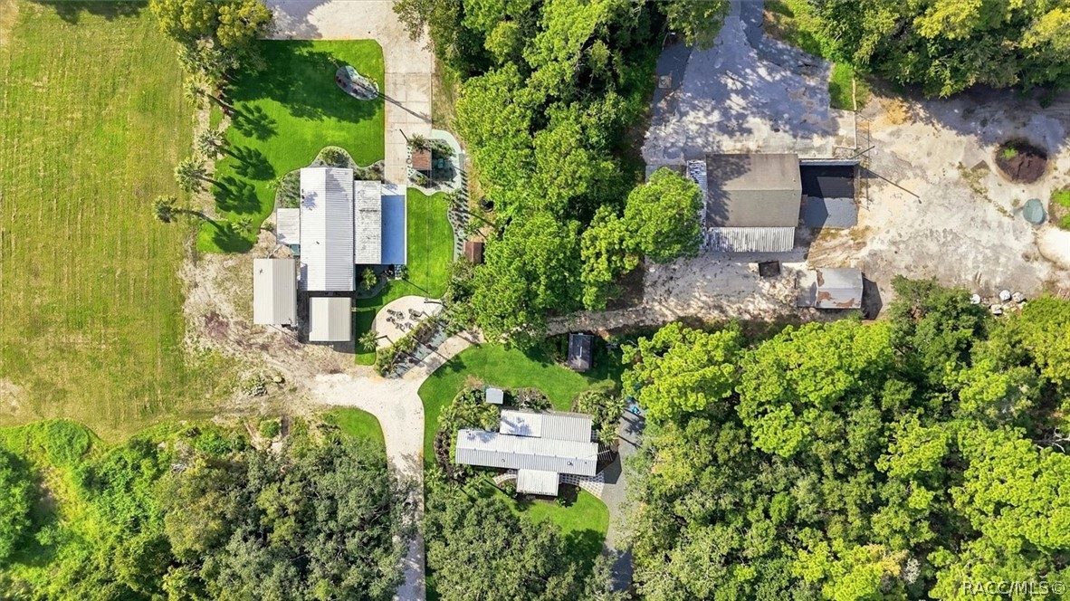 Aerial view of a home and outbuildings among lawns, trees, and a curved driveway.